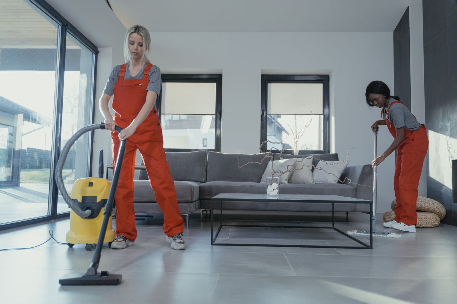 Two professional cleaners vacuuming and mopping a bright living room